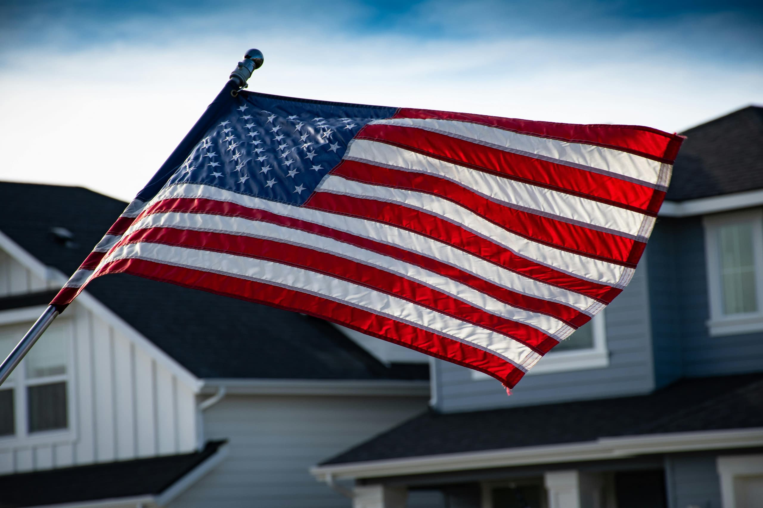 American flag waving in front of a suburban home, representing the pride of veterans and the benefits of VA Home Loans for achieving homeownership through a VA Loan