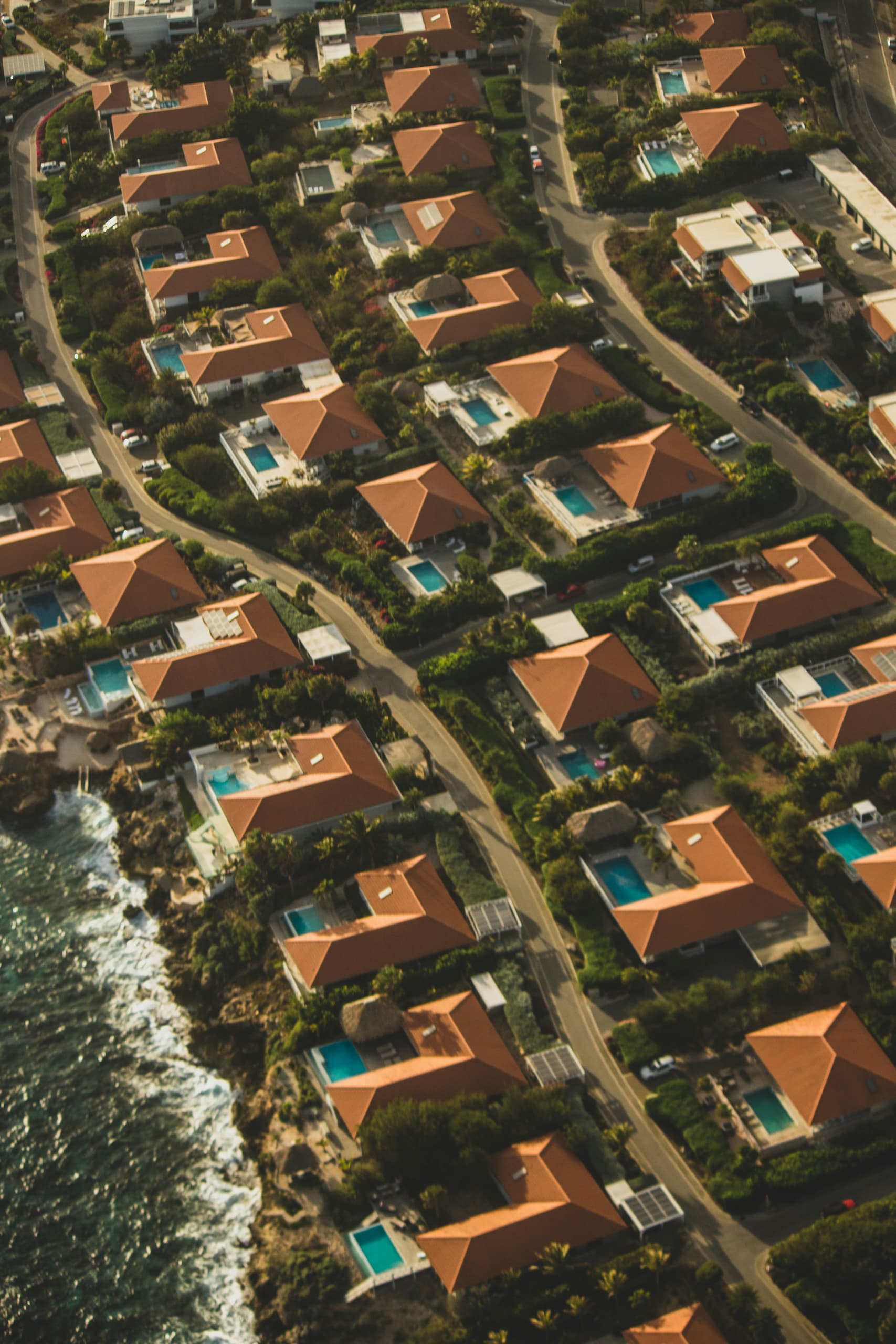 jorgen-hendriksen-5ed2_v8j74Q-unsplash (1) Aerial view of a coastal residential community with uniform homes, swimming pools, and landscaped streets, illustrating an HOA-managed neighborhood for homebuyers.